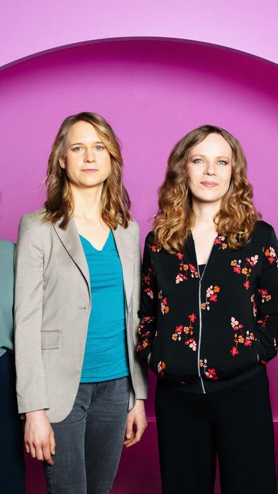 Auf dem Bild ist Sarah Bosetti als zweite von rechts zu sehen. Es sind vier Frauen auf dem Bild. Der Hintergrund ist rosa.