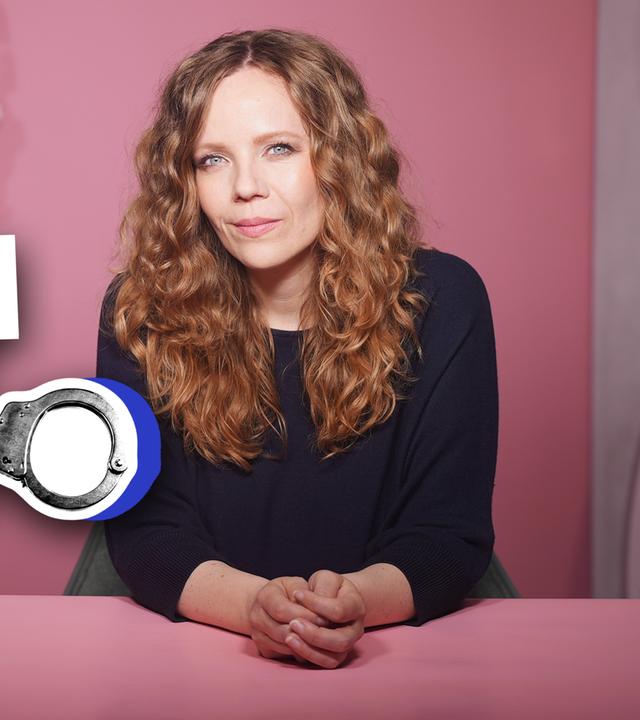 Sarah Bosetti sitzt rechts im Bild an einem rosa Tisch vor einem rosa Hintergrund. Links im Bild ist der Schriftzug "AfD KRIMINELLER ALS Zuwanderer?" zu sehen.