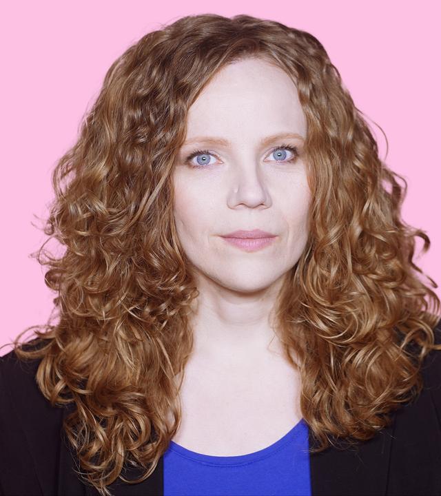Sarah Bosetti befindet sich vor einem rosa Hintergrund. Rechts von ihr in einer Blase ist Katherina Reiche zu sehen.