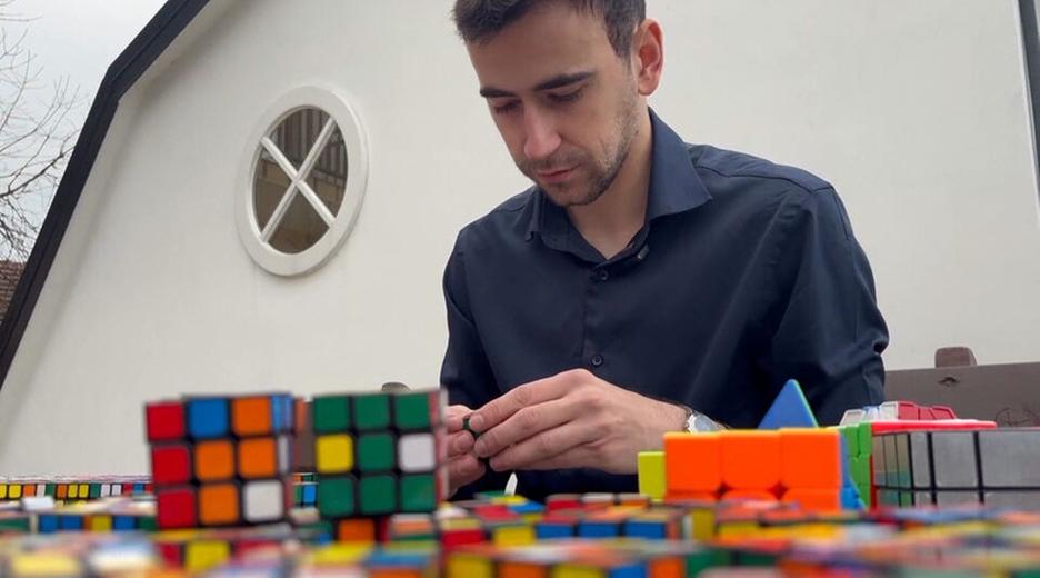 Ein Mann sitzt an einem Tisch mit vielen Rubik Cubes