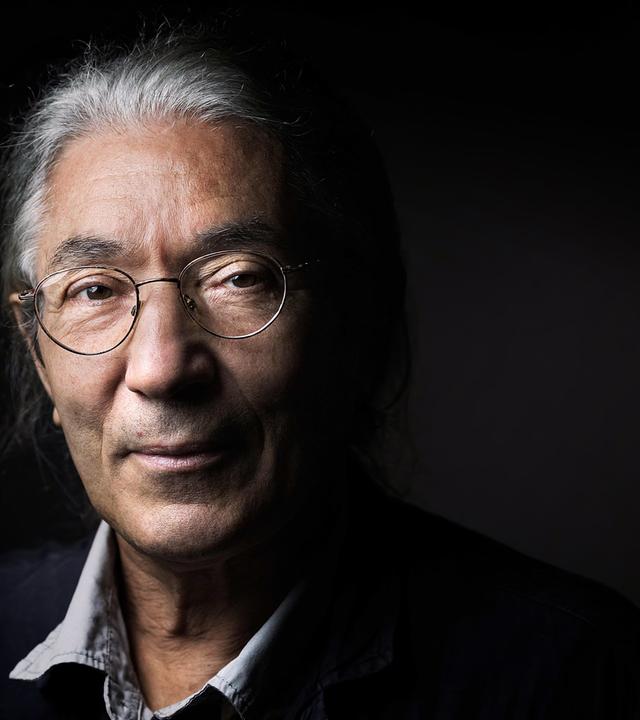 Porträtfoto eines Mannes mit grauen Haaren vor schwarzem Hintegrund.