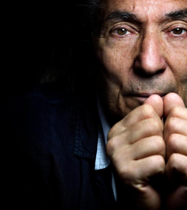 Nahaufnahme des Gesichts eines älteren Mannes der sich die Fäuste vor den Mund hält.