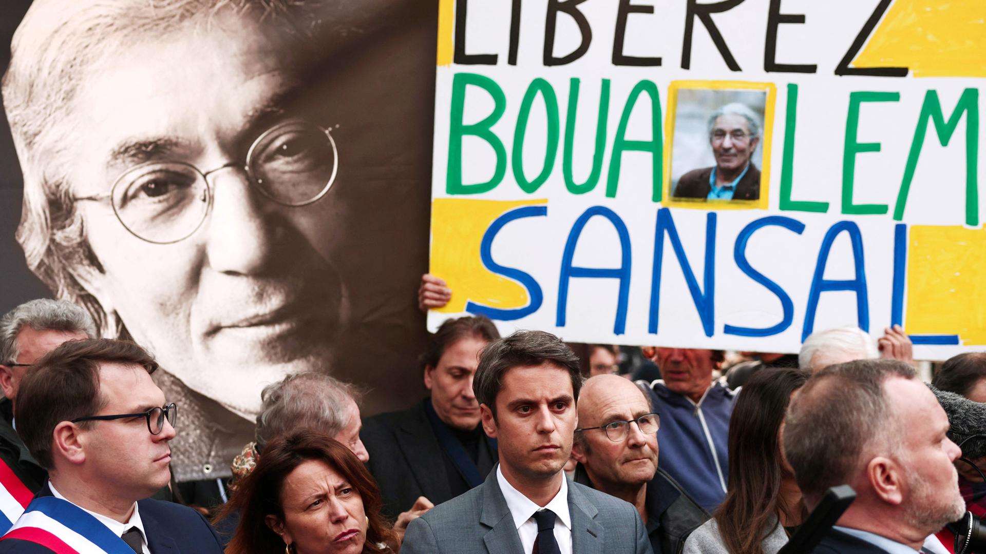 Menschen mit Plakaten stehen vor einem großen Bild des Schriftstellers.