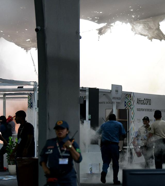 Rauch steigt nach einem Brand auf der Weltklimakonferenz empor. Viele Menschen stehen um den Ort des Geschehens.