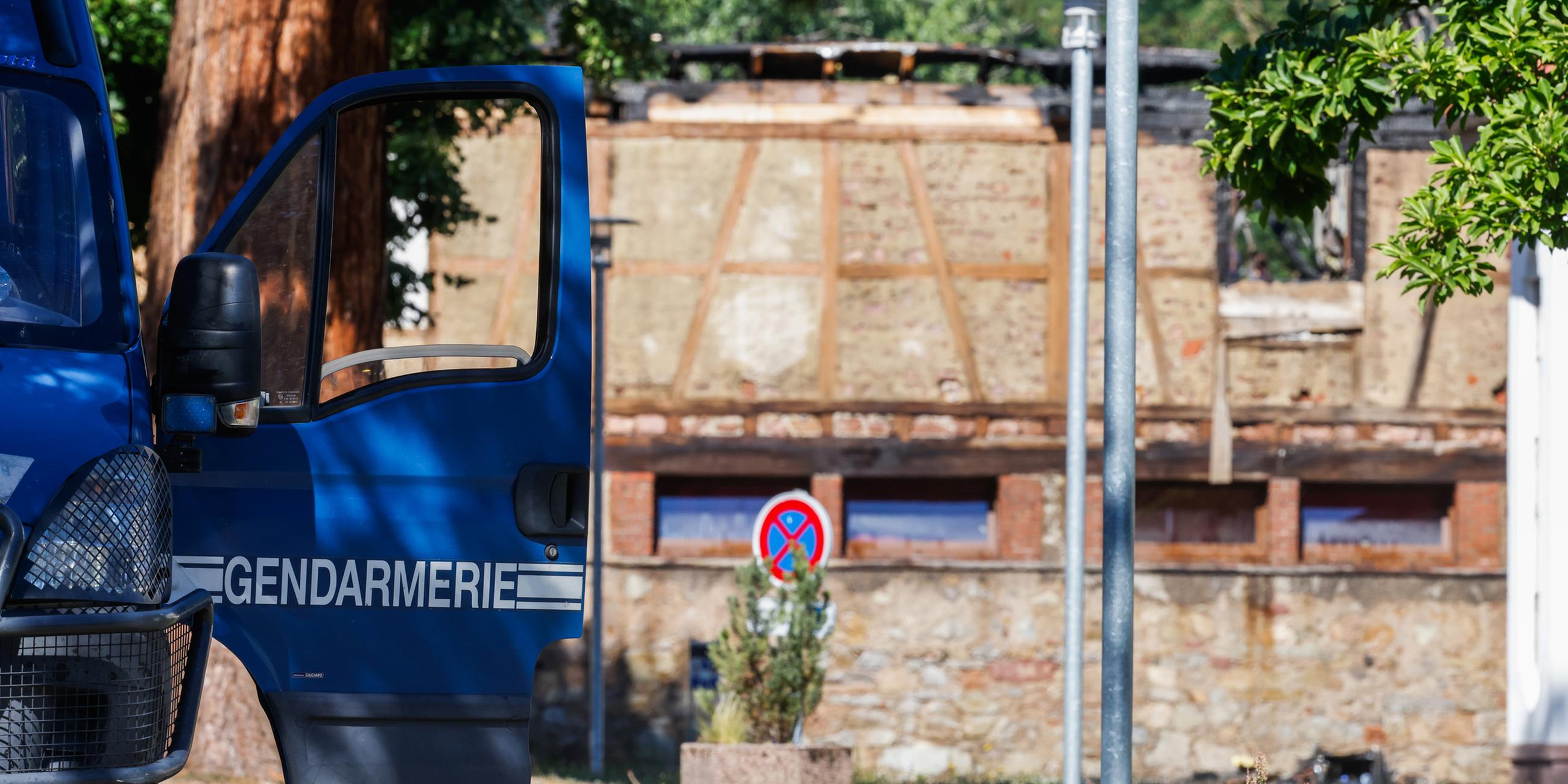 Die Tür eines Fahrzeugs der Gendarmerie steht offen, während im Hintergrund ein Haus zu sehen ist, in dem am Vortag bei einem Feuer elf Menschen ums Leben kamen. (10.08.2023)