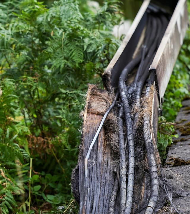 Polizist*innen vor verbrannten Kabeln in einem Kabelkanal.