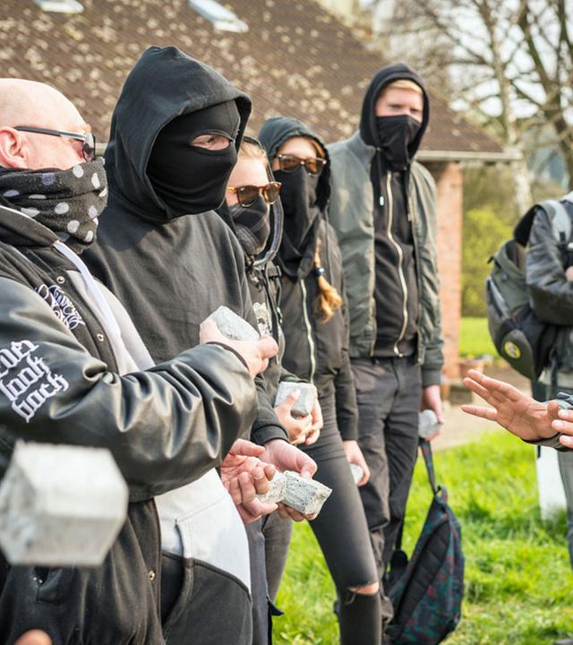"Notruf Hafenkante - Brandstifter": Der Polizist Tarik Coban (Serhat Cokgezen) steht, die Hände besänftigend hochhaltend, einer Gruppe vermummter Hooligans gegenüber.