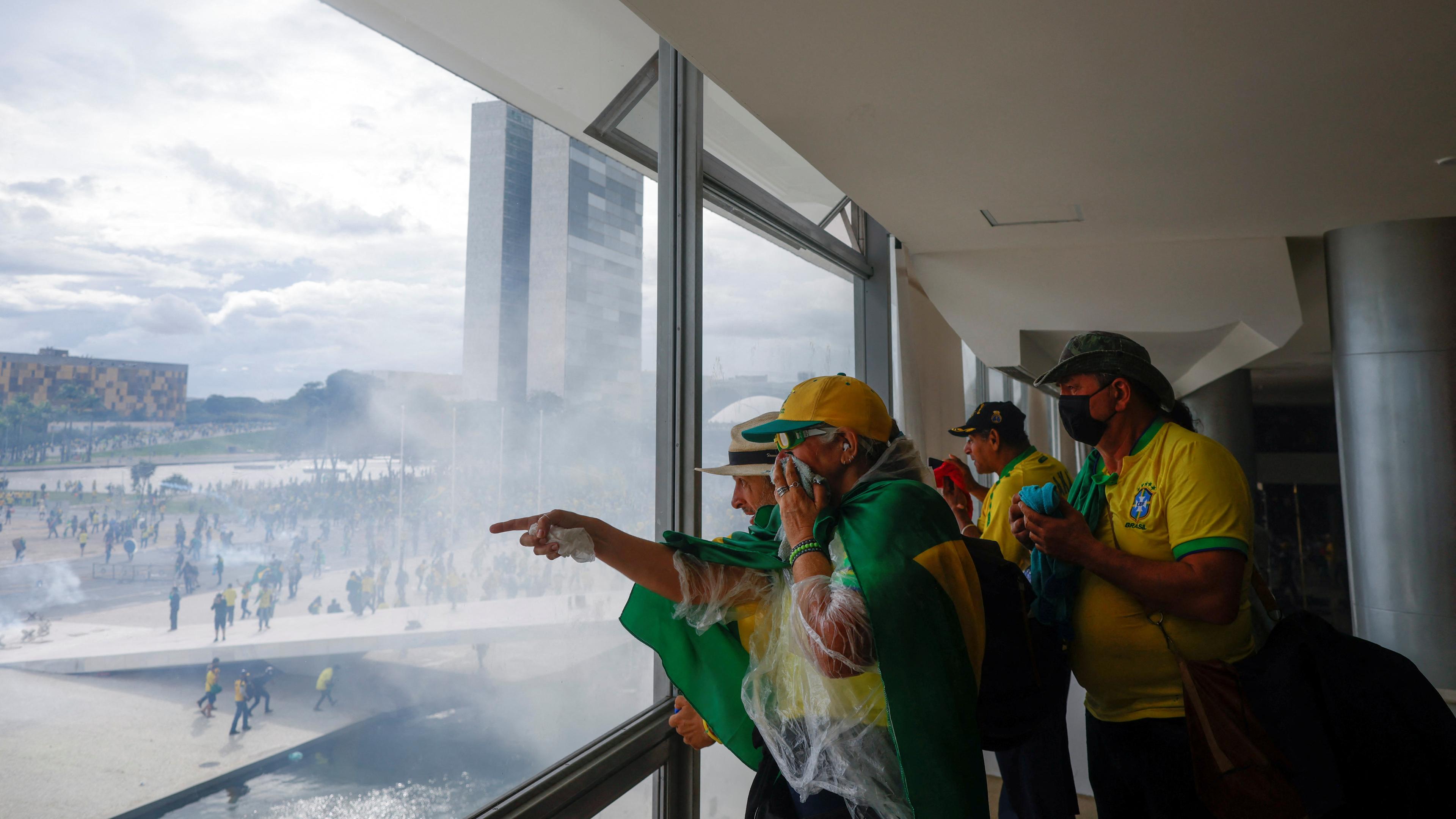 Bolsonaro-Anhänger stehen innerhalb des Kongresses in Brasilien und schauen aus dem Fenster. Draußen sind zahlreiche weitere Anhänger zu sehen.