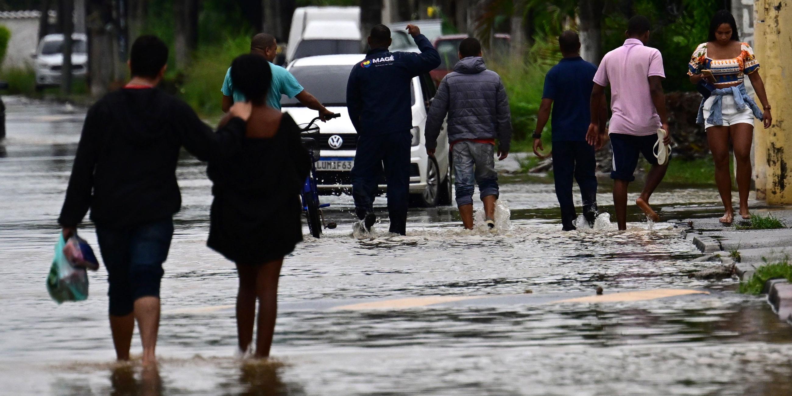 Archiv, 24.03.2024: Menschen waten durch eine überschwemmte Straße nach einem Regensturm im Stadtteil Uruai von Duque de Caxias am Rande von Rio de Janeiro in Brasilien.