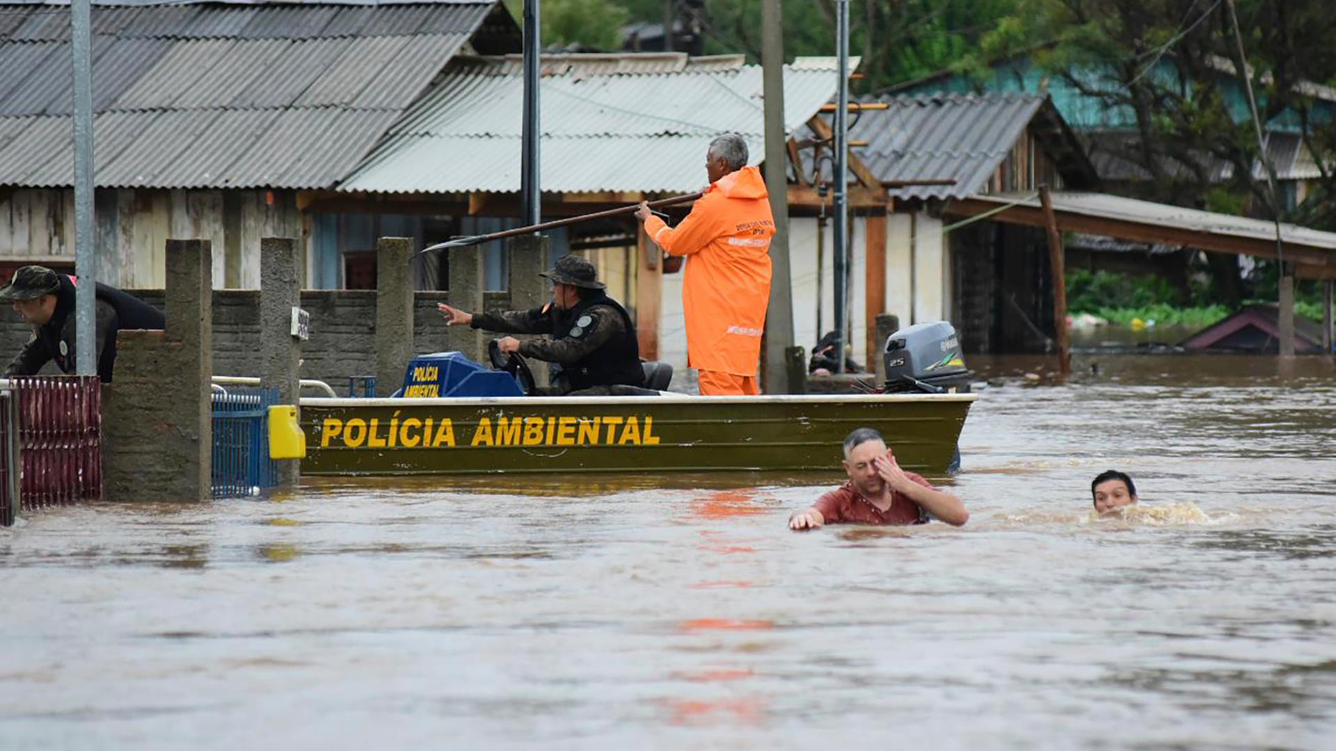  Polizeibeamte kontrollieren ein Haus, während Anwohner über eine überschwemmte Straße im Bundesstaat Rio Grande do Sul waten, nachdem ein Unwetter Überschwemmungen verursacht hat.