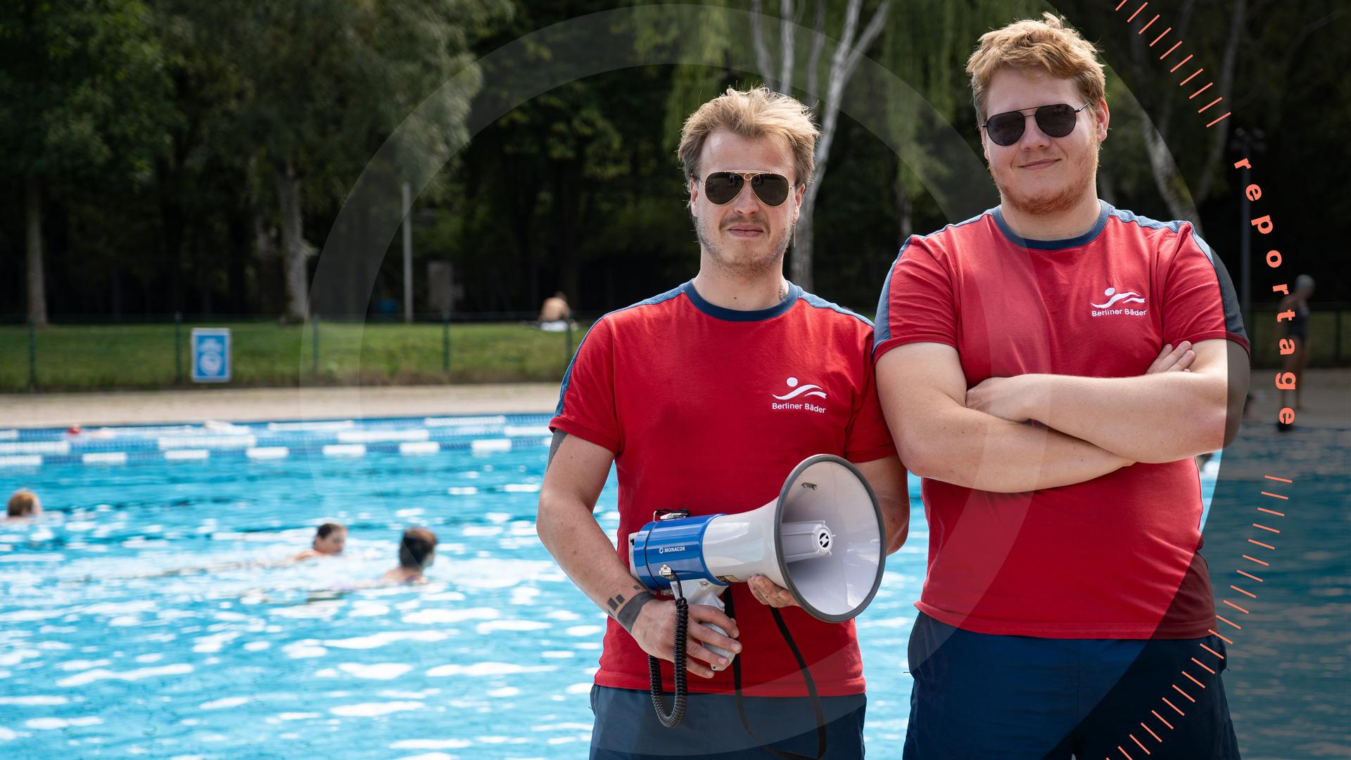 Pablo Spallek und sein Kollege Jakob stehen am Beckenrand eines Freibads. Beide tragen rote T-Shirts und blaue Shorts mit dem Logo der "Berliner Bäder" sowie eine Sonnenbrille. Pablo Spallek, hält ein Megafon in der Hand. Jakob, hat die Arme vor der Brust verschränkt. Im Hintergrund schwimmen Menschen im Wasser.