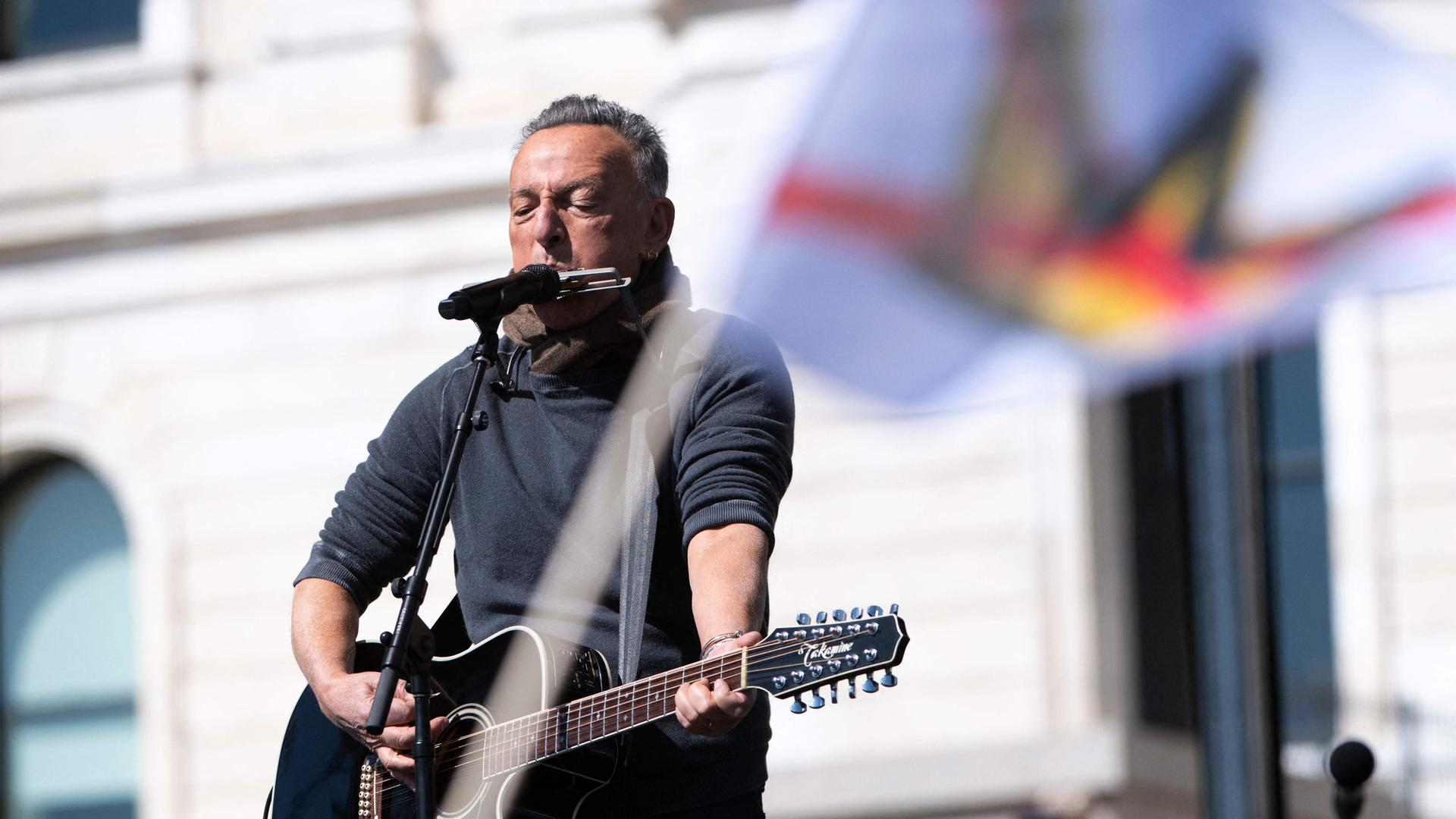 Mann spielt Gitarre und Mundharmonika, im Vordergrund Fahne mit durchgestrichener Krone.