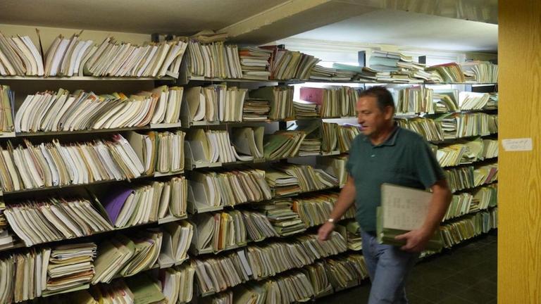 Ein Bote im Finanzamt zwischen Aktenbergen.