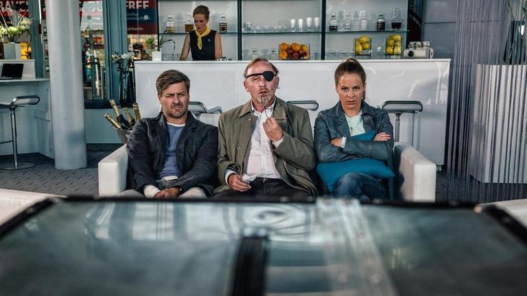 Die Kommissare Ludwig Schaller (Alexander Held, M.), Harald Neuhauser (Marcus Mittermeier, l.) und Angelika Flierl (Bernadette Heerwagen, r.) sitzen in der Flughafen-Lounge und warten darauf, die Diplomatin Victoria Sokol (Marion Mitterhammer) nun endg�ltig festzunehmen.