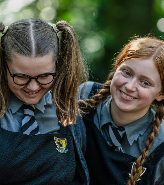 Mildred Hoppelt (Lydia Page, rechts), neben ihr steht Maude Mondschein (Meibh Campell, links) beide lachen