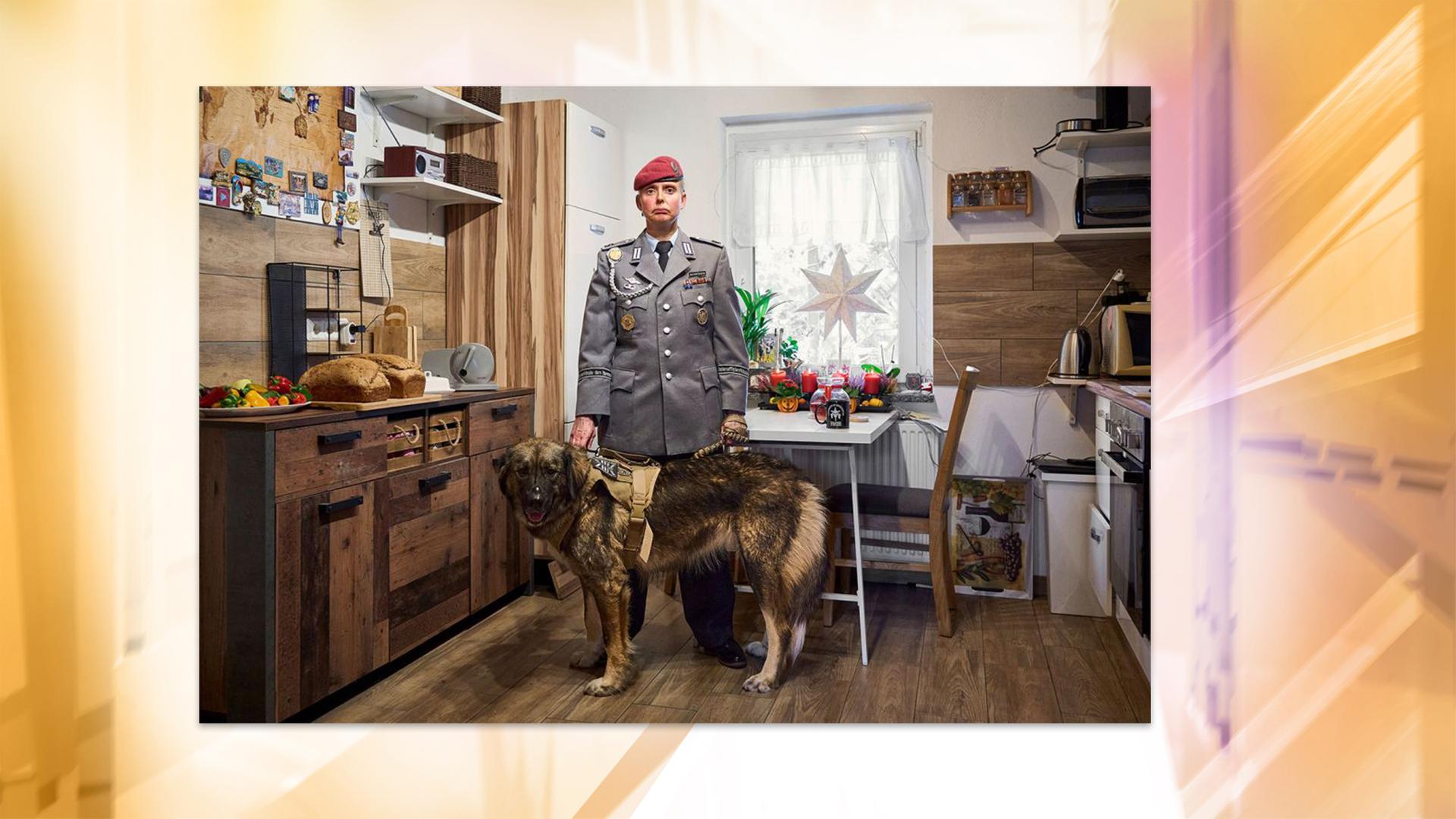 Man sieht eine Soldatin in Uniform mit einem Hund in einer Küche stehen.
