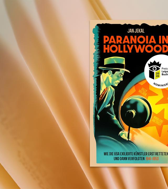 Ein Mann in Anzug und mit Hut, der eine Lampe hält und damit auf eine Wand leuchtet. Dort sind Sterne wie beim Hollywood Walk of Fame zu sehen.