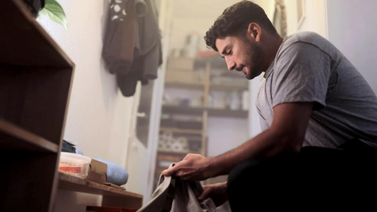 Szene aus "Hund, Wolf, Schakal" von Behzad Karim Khani. Ein junger Mann kniet in einem Flur und hält eine Decke in den Händen. Er hat einen besorgten Gesichtsausdruck.