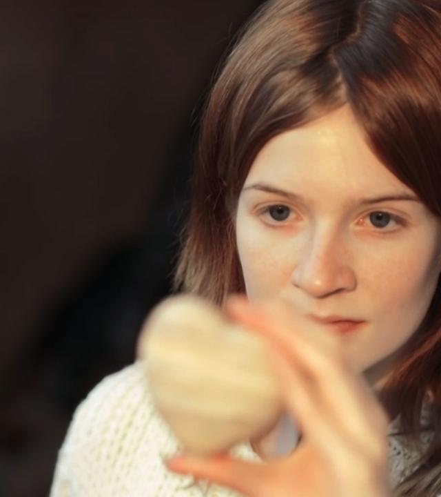 Szene aus "Der ganze Himmel" von Trent Dalton. Eine junge Frau hält ein Herz aus Stein auf Kinnhöhe in ihrer linken Hand und betrachtet es nachdenklich.