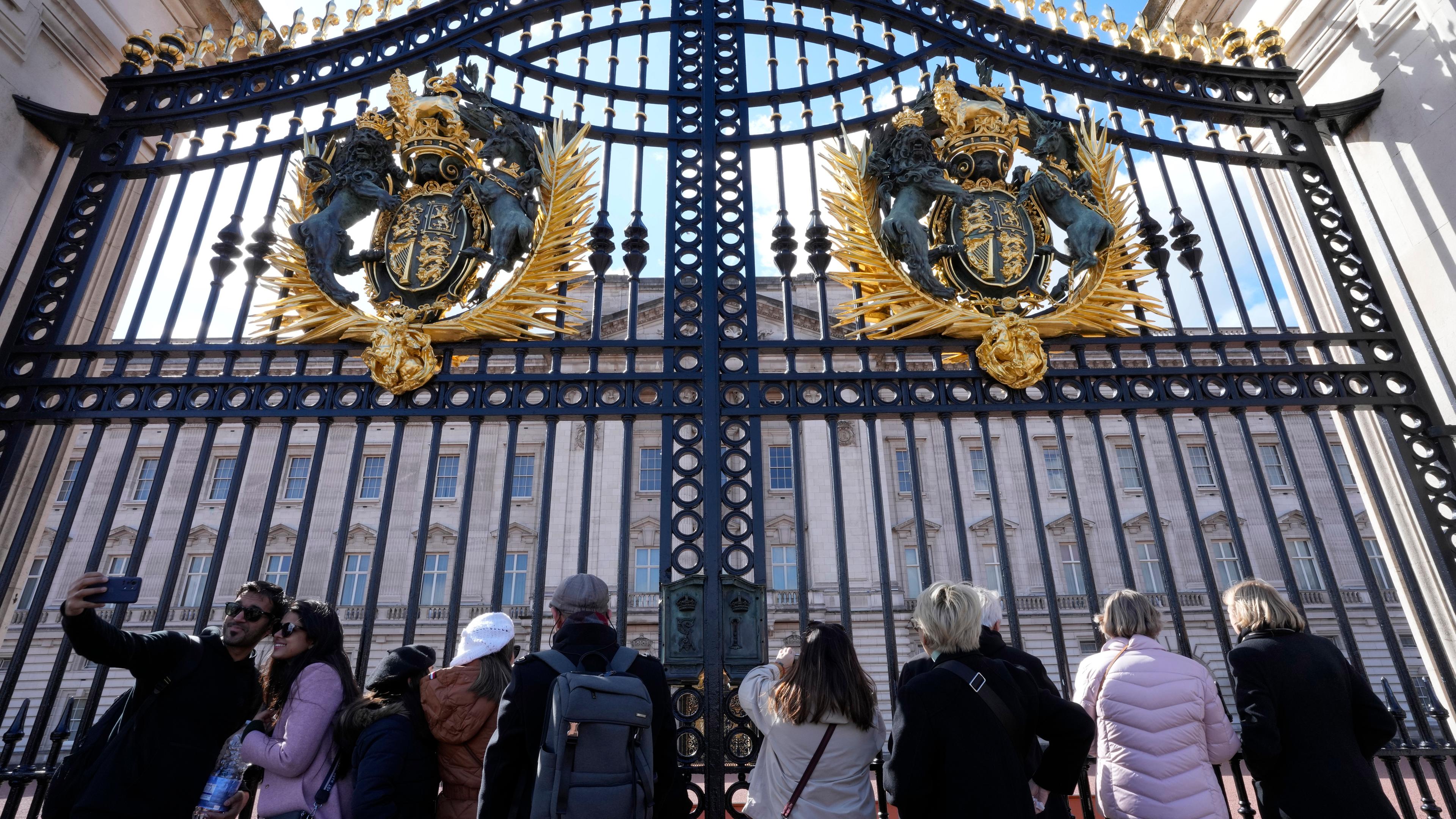 Touristen posieren am 24. 03. 2024, vor den Haupttoren des Buckingham Palasts in London für ein Foto. 