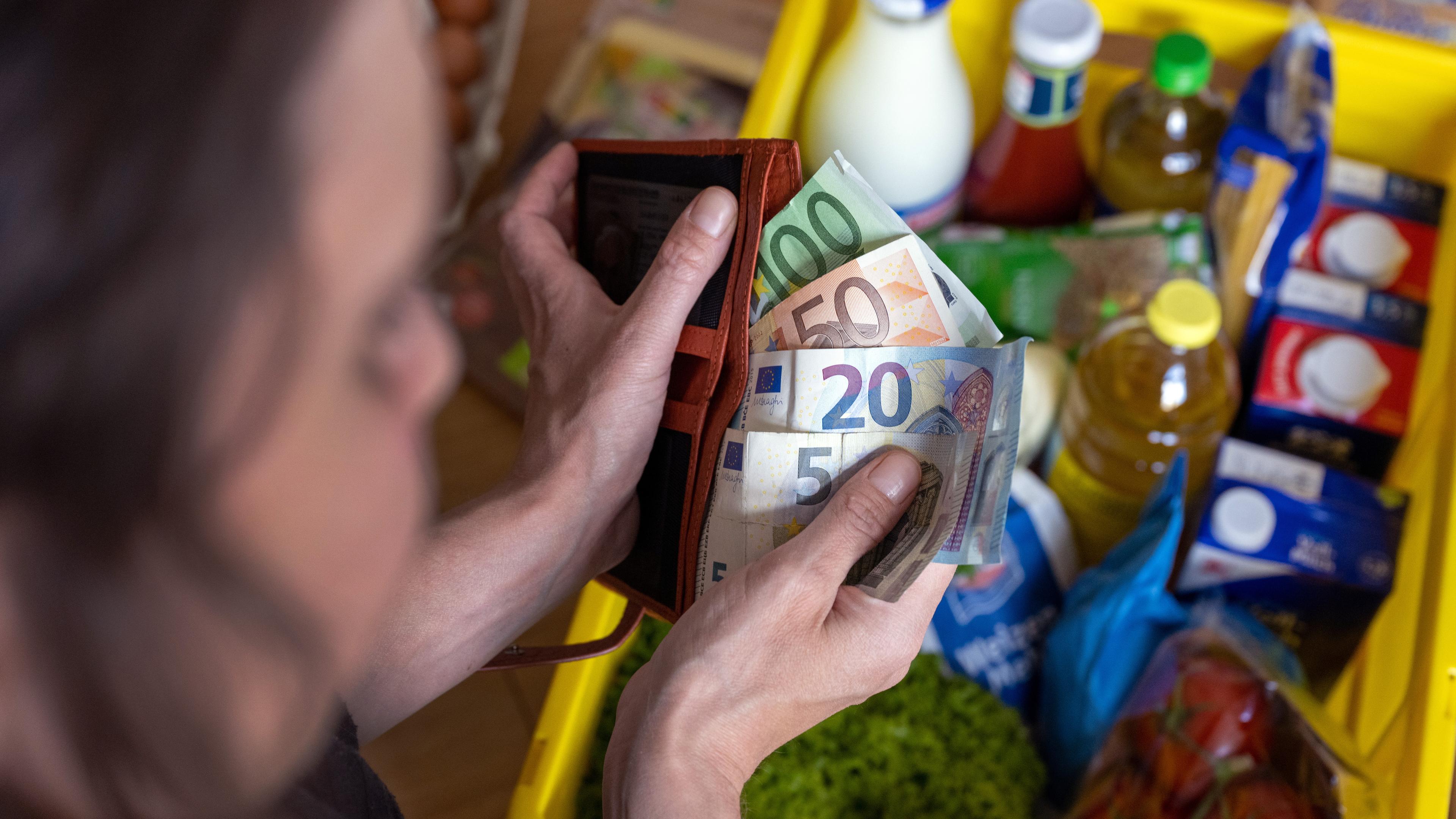 Eine Frau hält Geldscheine in einer Geldbörse über einer Einkaufskiste mit Lebensmitteln, der auf einem Küchentisch in Leipzig steht,  aufgenommen am 02.06.2022