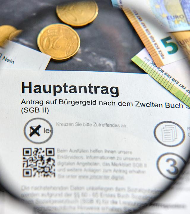 Hand hält Lupe über das Wort Bürgergeld auf dem Hauptantrag auf Bürgergeld der Agentur für Arbeit