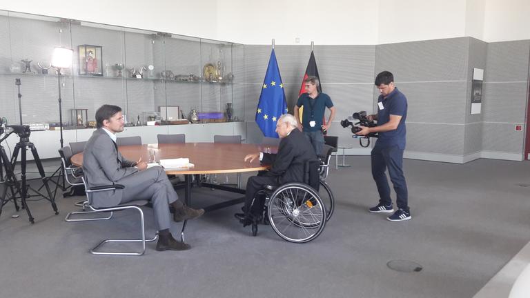 "ZDFzoom: Geheimakte Finanzkrise - Droht der nächste Jahrhundert-Crash?": Autor Dirk Laabs sitzt mit Wolfgang Schäuble an einem Tisch und unterhält sich mit ihm. Daneben sind zwei Männer vom Filmteam zu sehen.