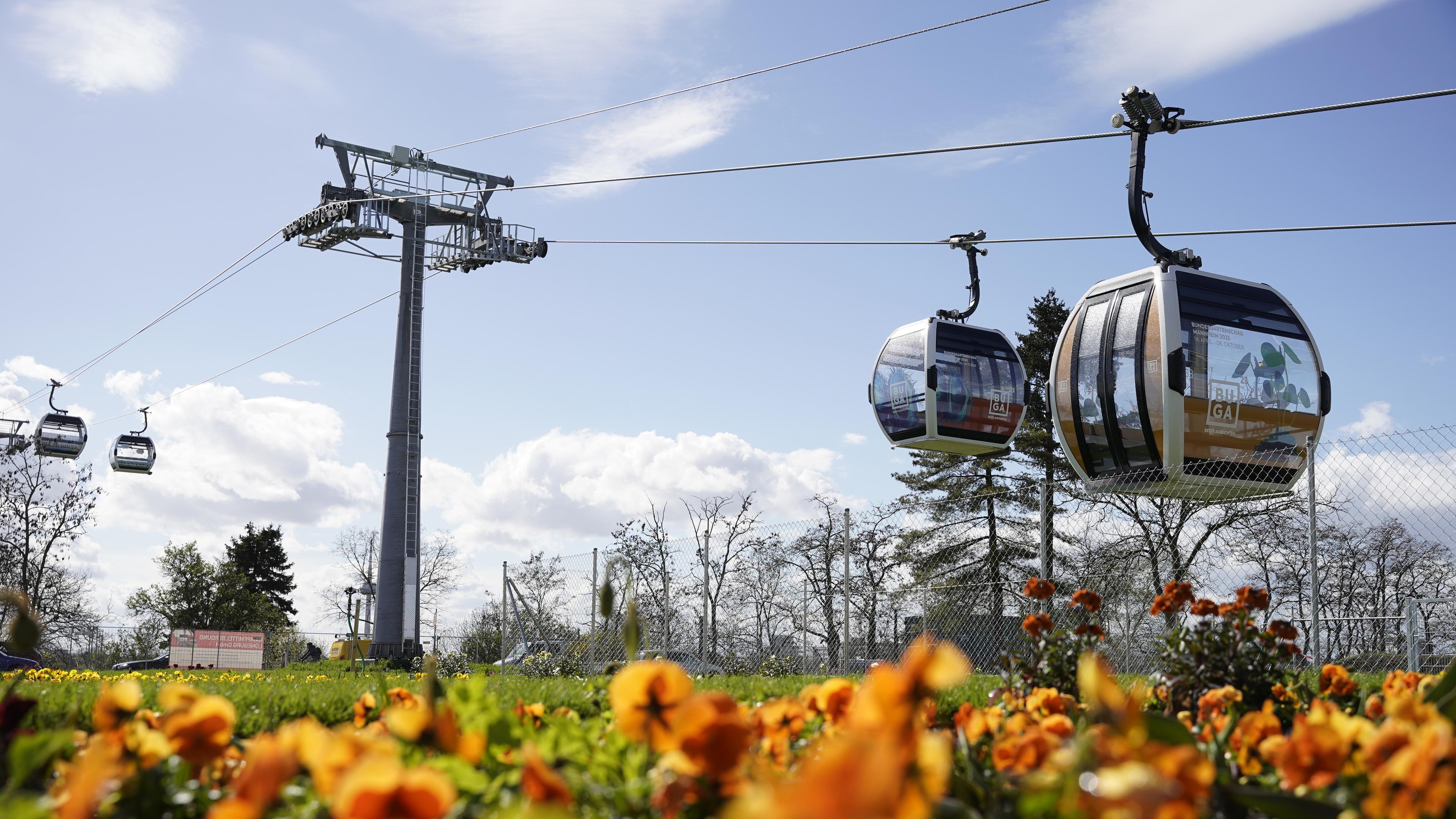 BundesgartenschauKabinen der Seilbahn fahren auf dem Gelände der Bundesgartenschau hinter einem Blumenbeet.