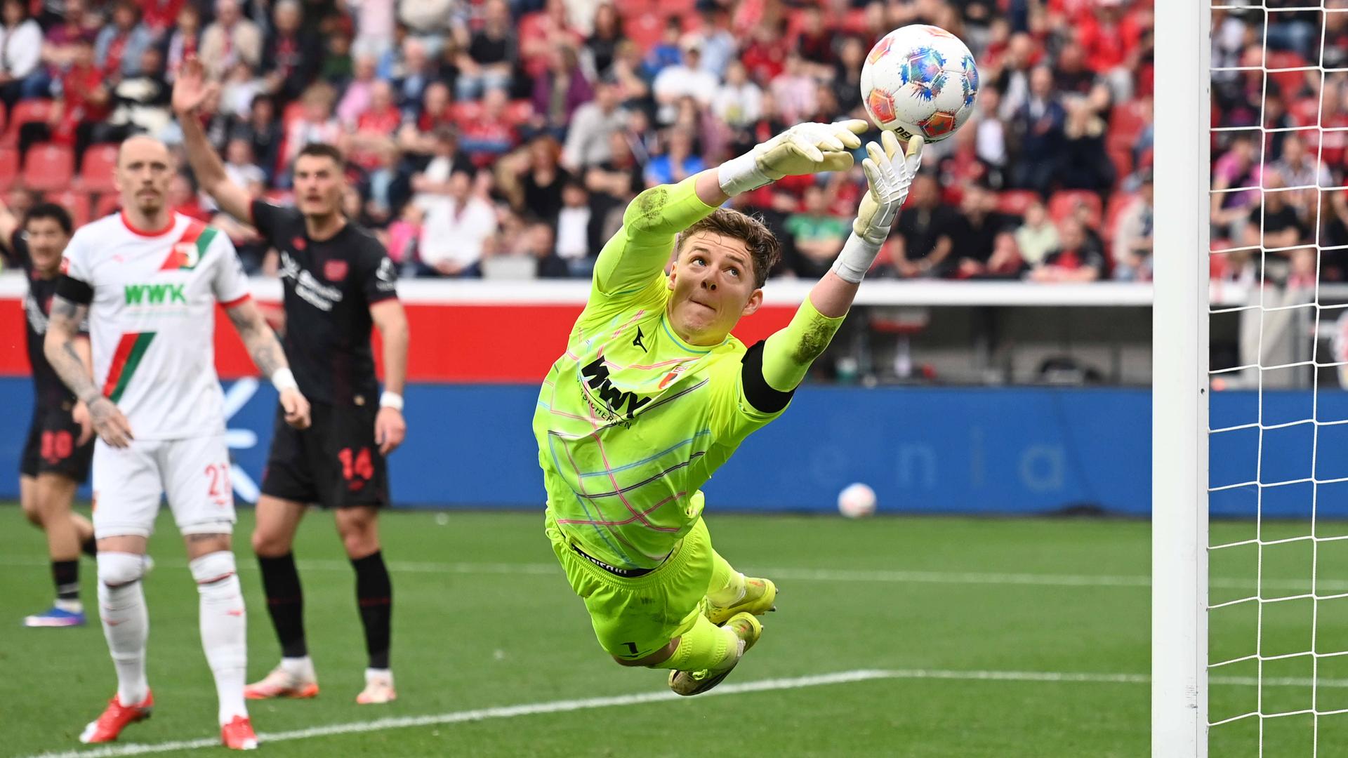 Parade von Torwart Finn Dahmen (FC Augsburg) am 18.04.2026 in Leverkusen.