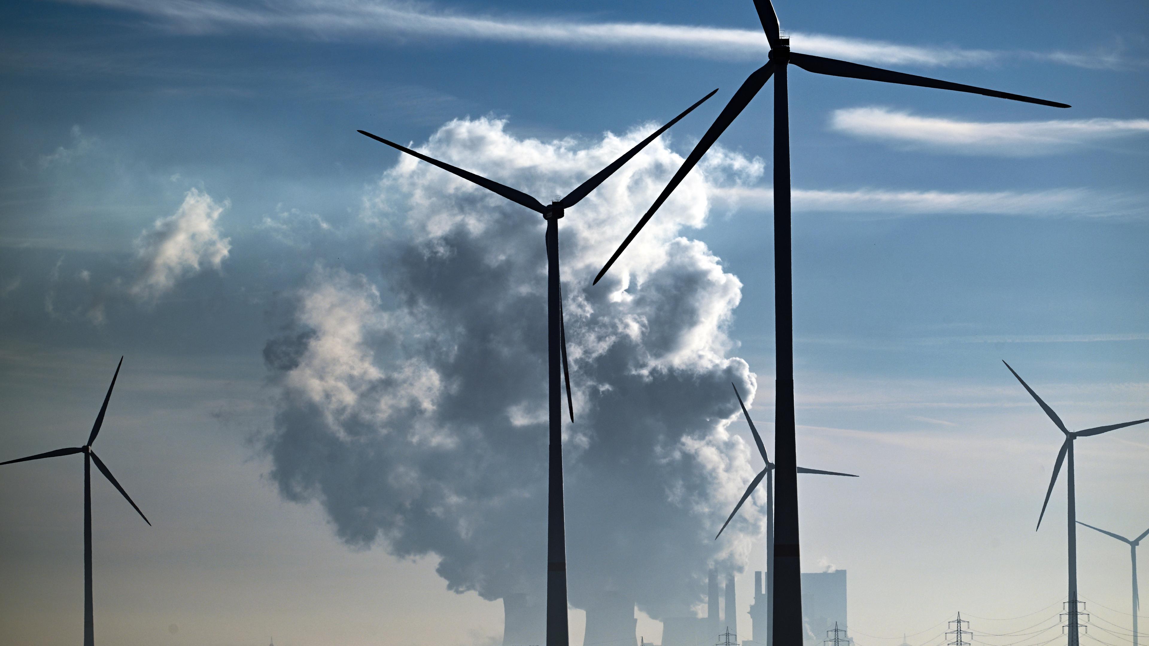 Windkrafträder im Vordergrund. Im Hintergrund steigt Rauch aus dem Braunkohlekraftwerk Neurath auf.