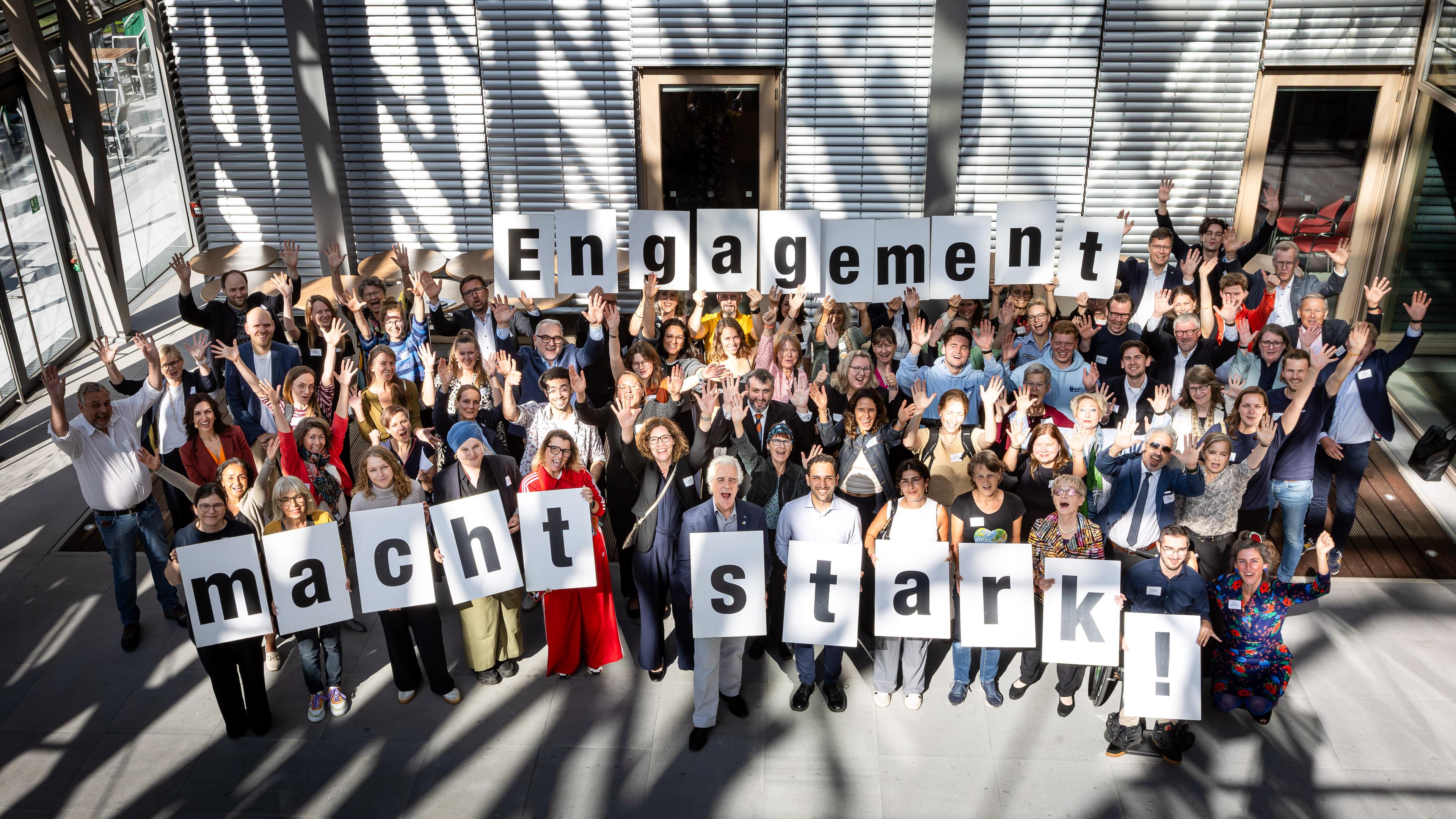 Eine Menschenmenge des Treffens des Bürgerschaftlichen Engagements (BBE) aus der Vogelperspektive hält Buchstabenschilder zum Schriftzug "Engagement macht stark" hoch