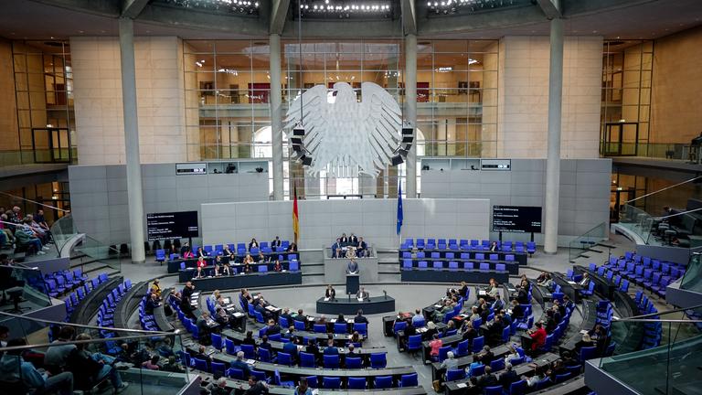 Deutscher Bundestag. Vogelperspektive des Saals. Der Bundesadler und einige Abgeordneten sind zu sehen.