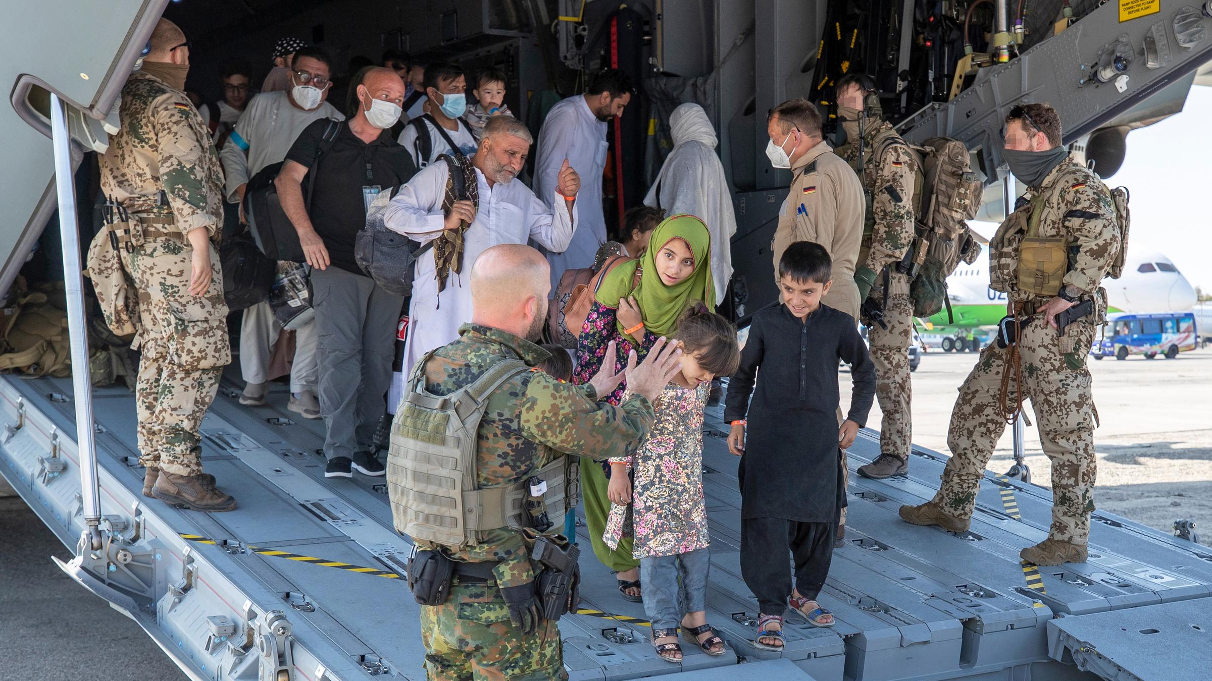 Bundeswehrsoldaten begleiten aus Afghanistan ausgeflogenen Menschen aus einem Flugzeug heraus, 18.08.21, Taschkent.