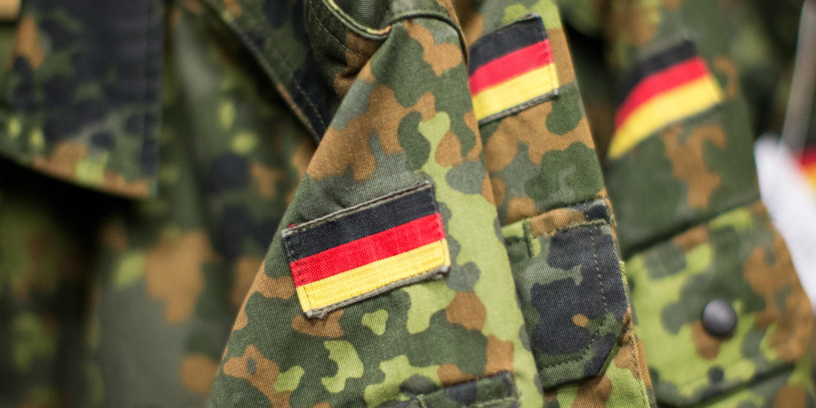 Uniform-Jacken der Bundeswehr mit ansgenähter Deutschlandflagge hängen an einer Garderobe. 