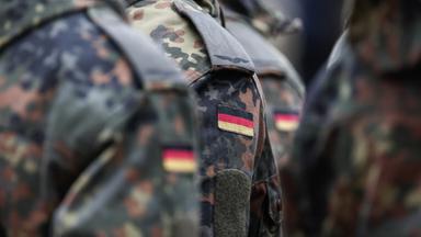 Die aneinandergereihten Schultern von uniformierten Bundeswehrsoldat:innen mit der deutschen Fahne.