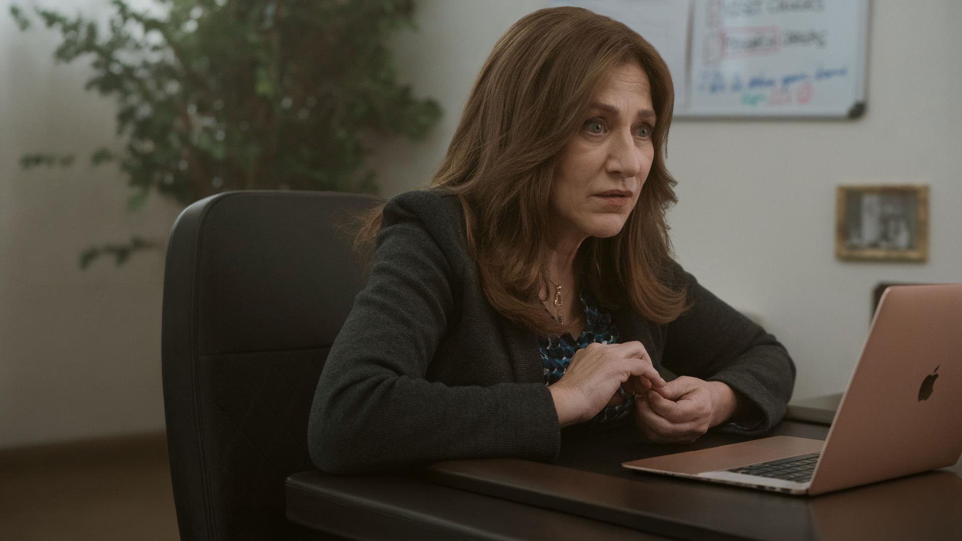 "Bupkis - Crispytown": Amy Davidson (Edie Falco) sitzt, mit grünem Jackett und an den Nägeln kribbelnd, am Laptop. Sie wirkt schockiert.