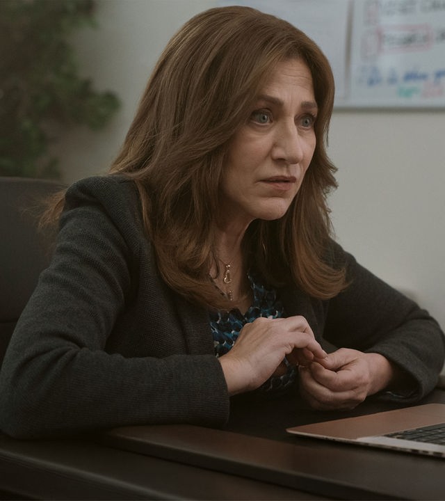 "Bupkis - Crispytown": Amy Davidson (Edie Falco) sitzt, mit grünem Jackett und an den Nägeln kribbelnd, am Laptop. Sie wirkt schockiert.