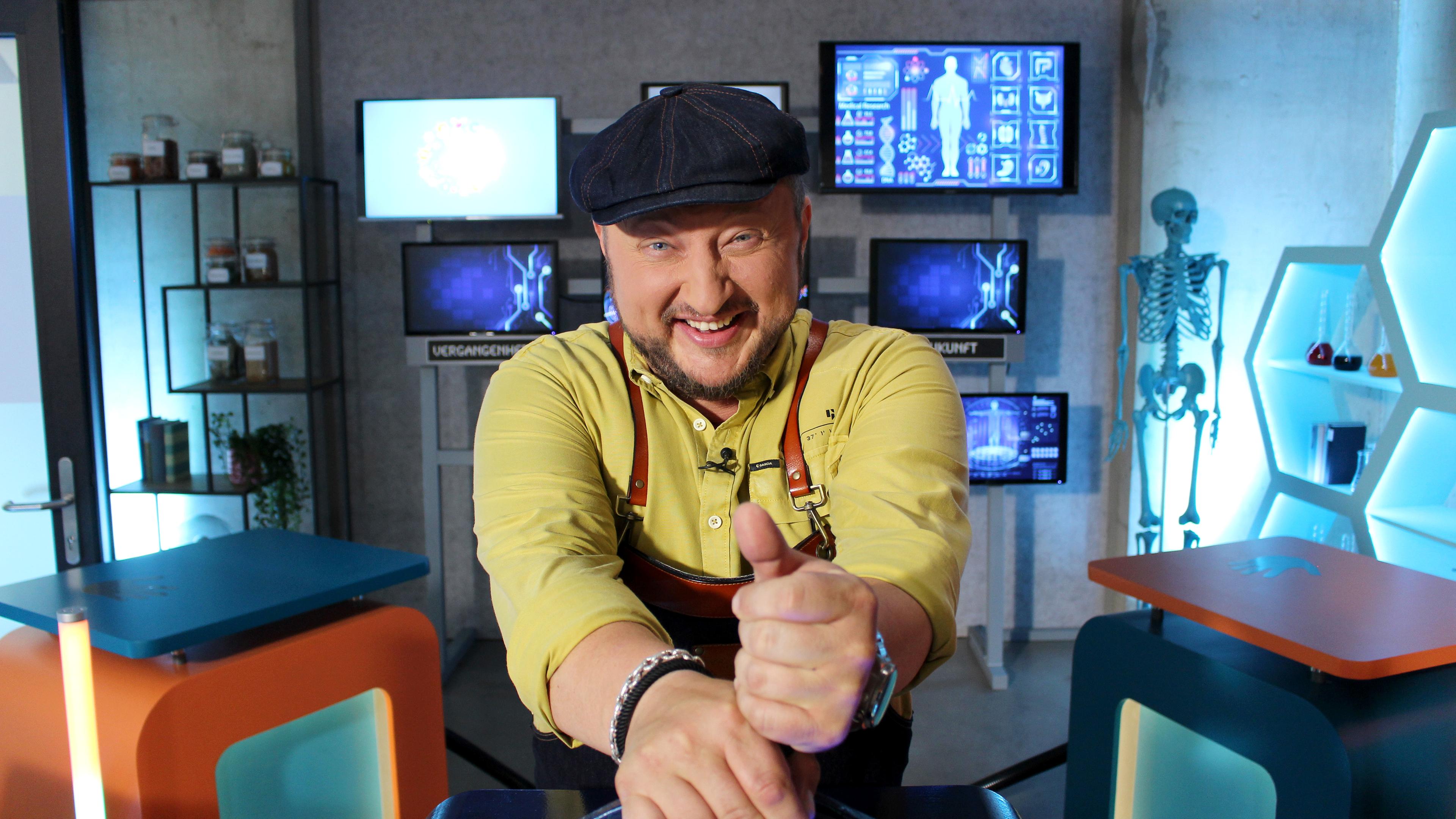 Ein Mann sitzt mit Daumen hoch in einem Studio.