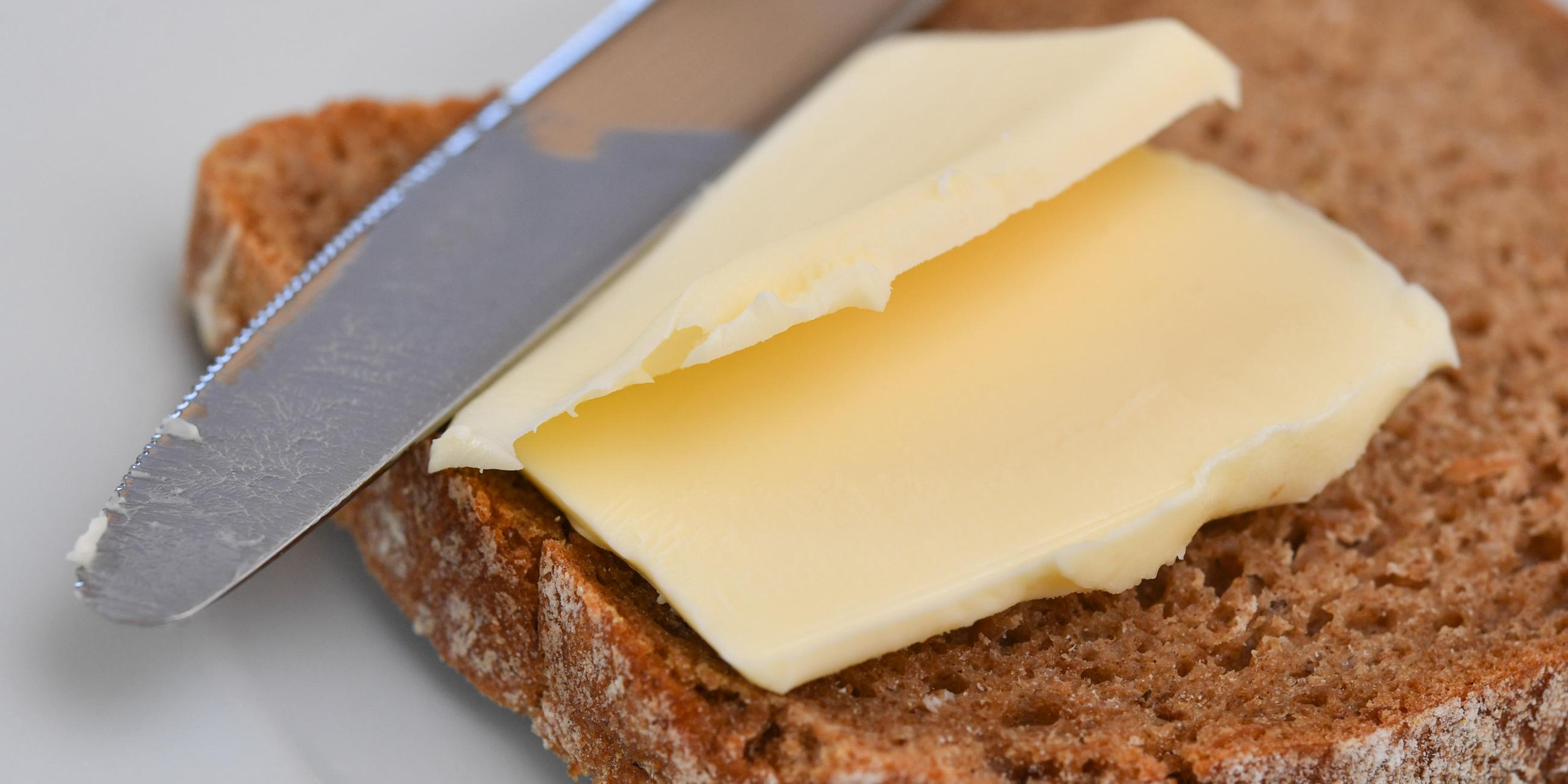 Eine Brotscheibe mit Butter liegt mit einem Messer auf einem Teller 
