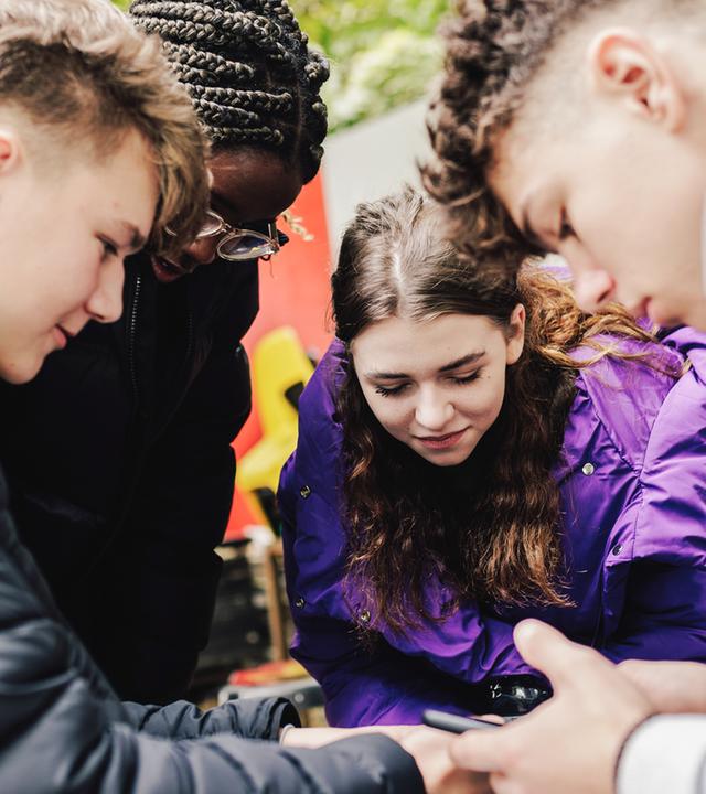 Diana, Anton, Ros und Dasha stehen im Kreis und schauen auf ein Handy