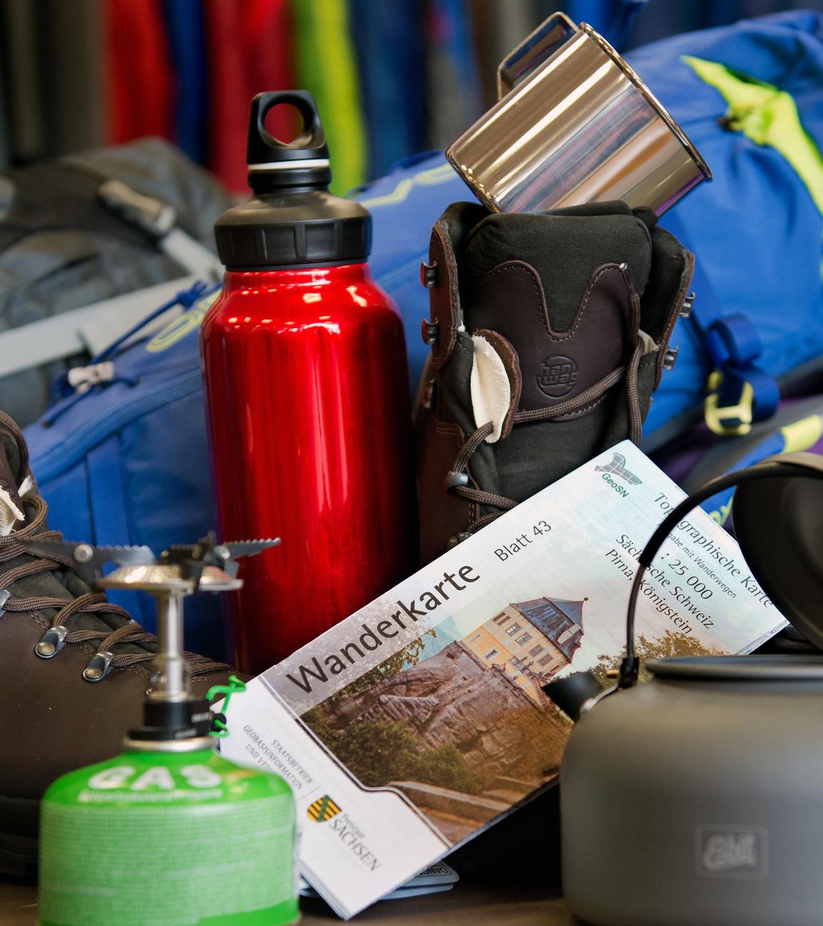 Verschiedene Dinge wie Becher, Trinkflasche oder Gaskocher, die für Wander- und Campingausrüstung notwendig sind.