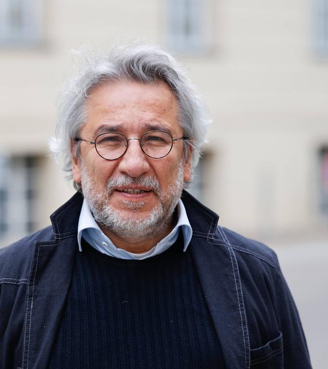 Foto eines Mannes mit weißen Locken, graumeliertem Bart und runder Metall-Brille.