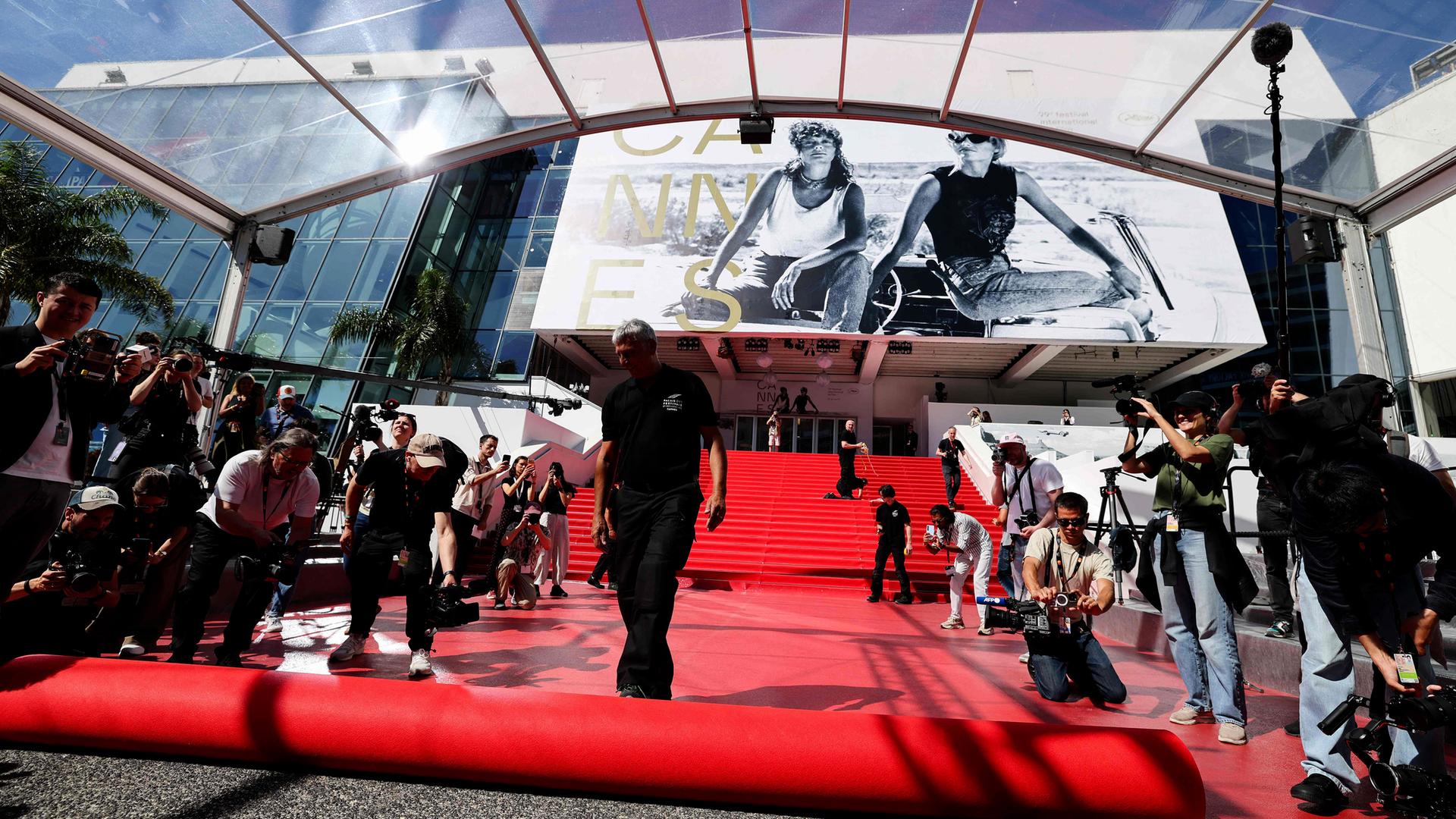 Pressefotografen und Zuschauer machen Fotos, während der rote Teppich vor dem Eingang zum Kino in Cannes ausgerollt wird.