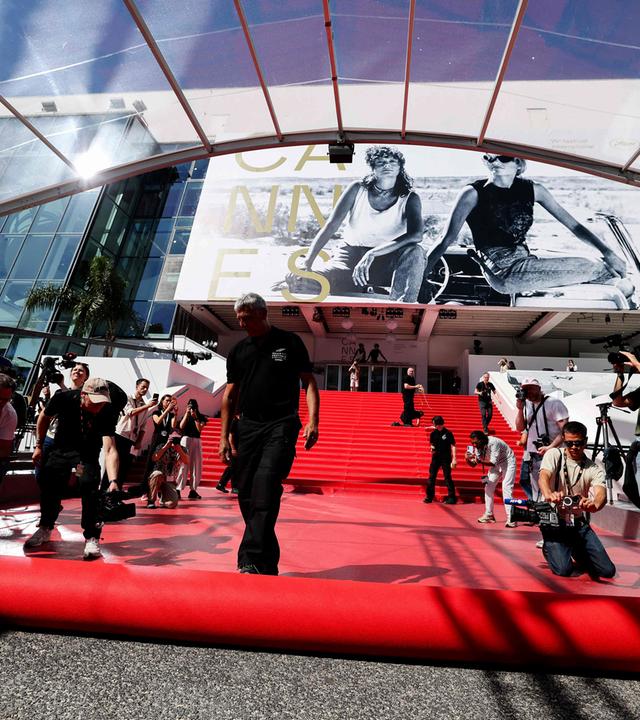Pressefotografen und Zuschauer machen Fotos, während der rote Teppich vor dem Eingang zum Kino in Cannes ausgerollt wird.