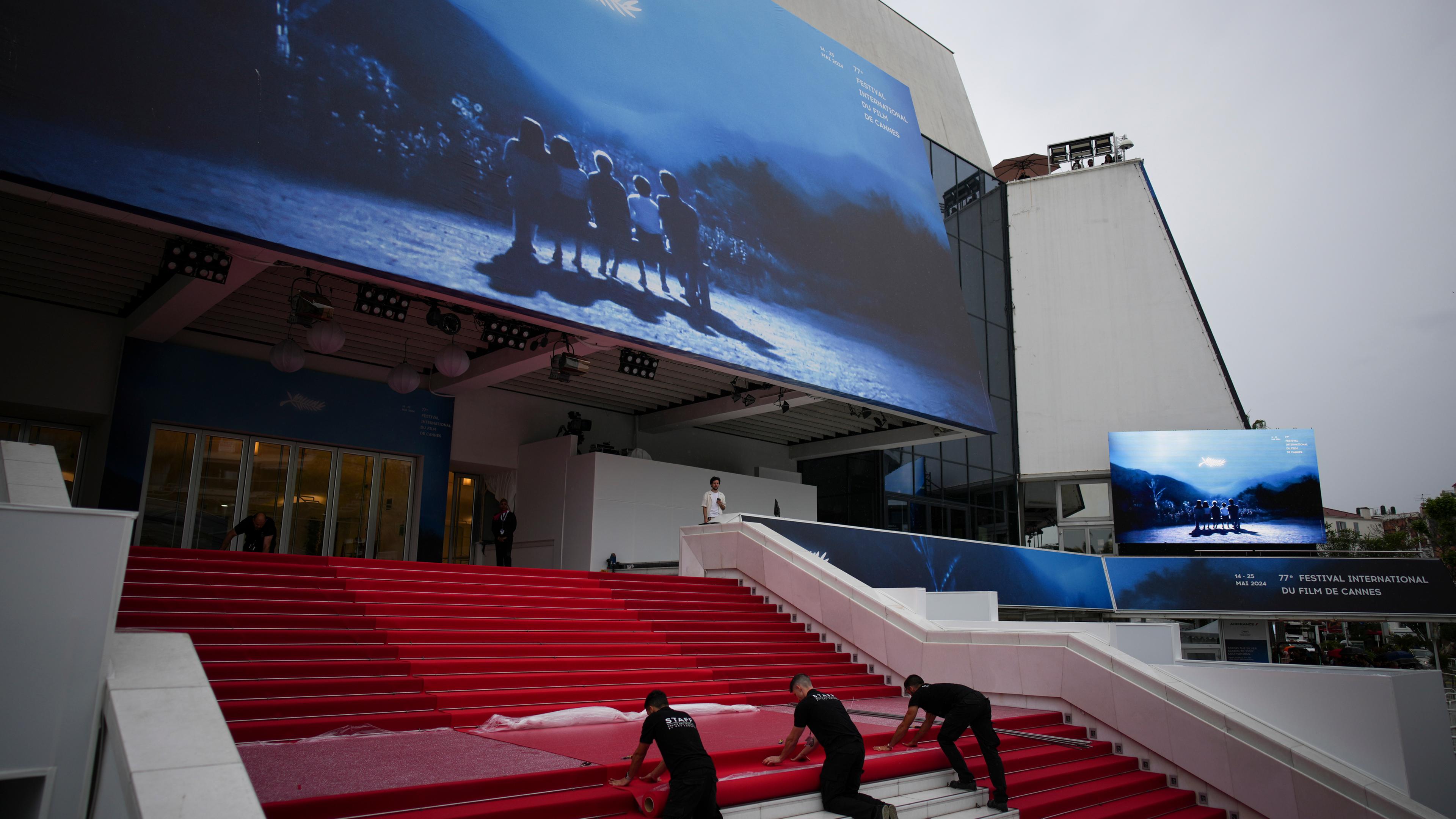 Festivalmitarbeiter legen am Eröffnungstag des 77. Internationalen Filmfestivals in Cannes den roten Teppich im Palais des Festivals aus.