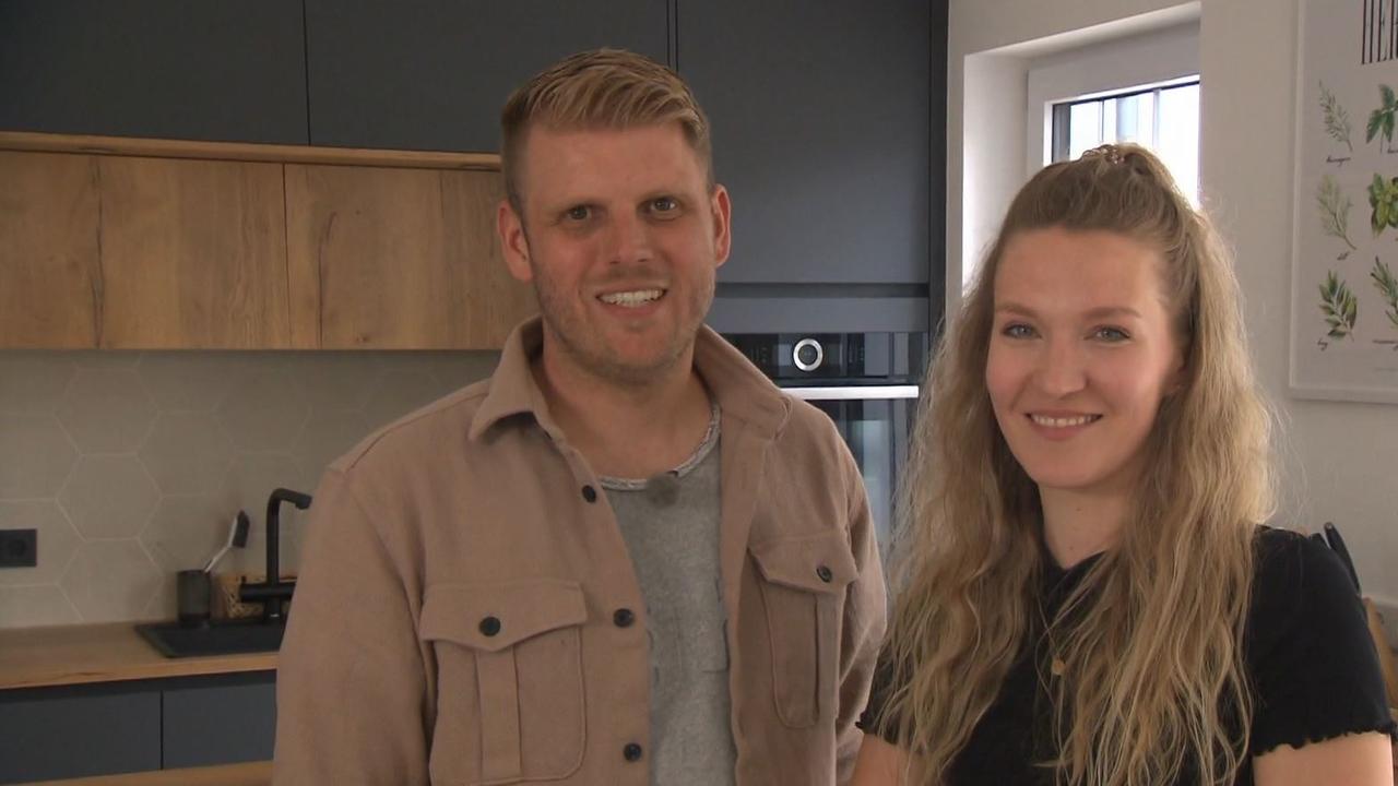 Carina und Johannes Sterner stehen lächend in ihrer Küche und schauen in die Kamera. 