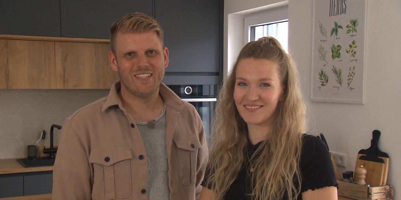 Carina und Johannes Sterner stehen lächend in ihrer Küche und schauen in die Kamera. 