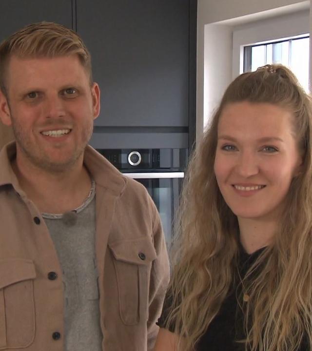 Carina und Johannes Sterner stehen lächend in ihrer Küche und schauen in die Kamera. 