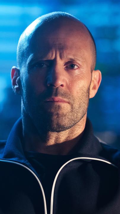 Patrick Hill (Jason Statham) sitzt vor einem mit Rollladen abgedunkeltem Fenster und schaut in die Kamera.