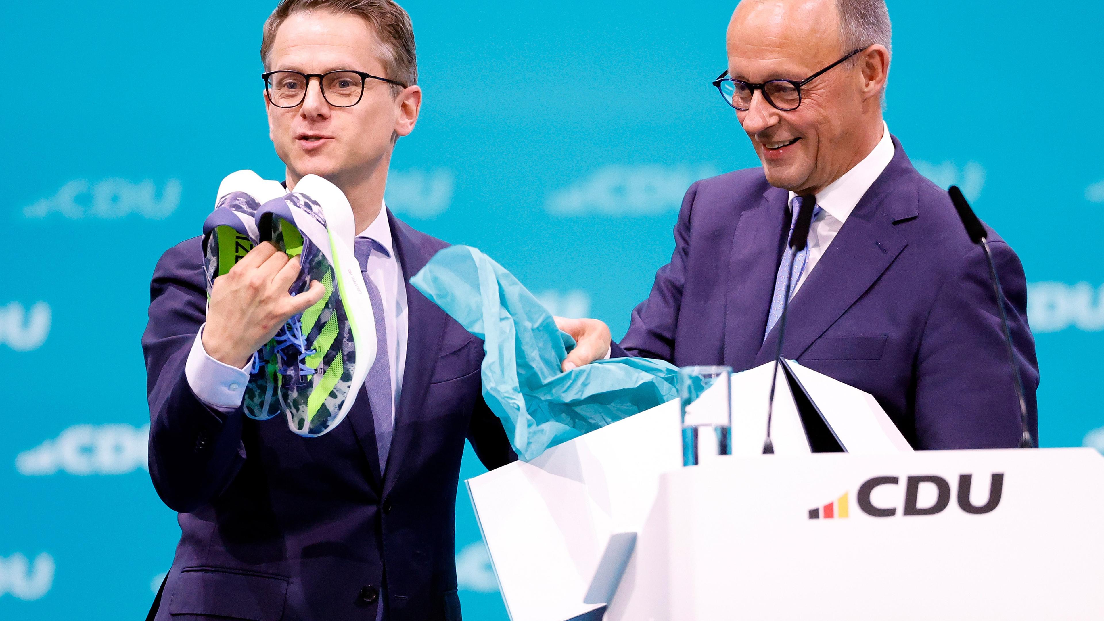 Berlin: Carsten Linnemann (l), CDU Generalsekretär, hält Laufschuhe in der Hand, nachdem sie ihm von Friedrich Merz, CDU Bundesvorsitzender, beim CDU-Bundesparteitag überreicht wurden.